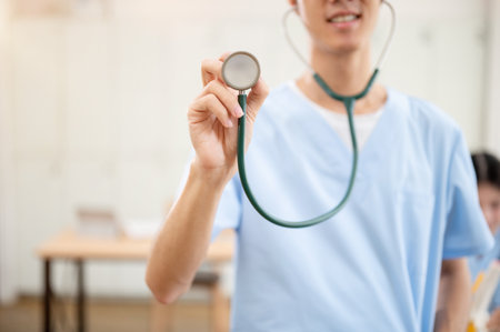 A close-up of a male doctor in scrubs, showing his stethoscope to the camera while standing in a clinic. medical school, medical, health care, hospitalの写真素材