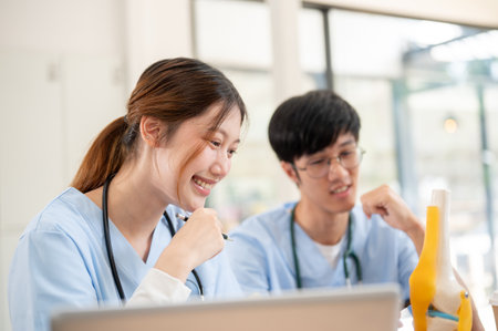 A beautiful, smart Asian female medical student in scrubs is examining a model of bone joints and...