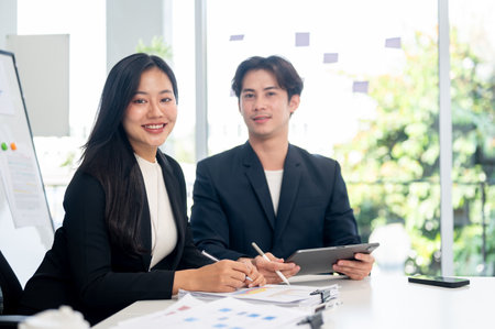 An Asian businesswoman in a business suit sits at a meeting table in the meeting room, smiling at the camera.の写真素材