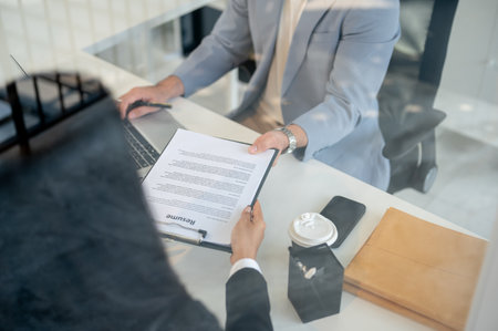 A close-up of a female candidate handing her resume to a CEO during an interview in the office. job interview, recruitment, careerの写真素材