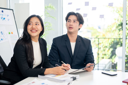 Two positive and smart Asian businesspeople are intently listening to a presentation during a meeting. business meeting conceptの写真素材