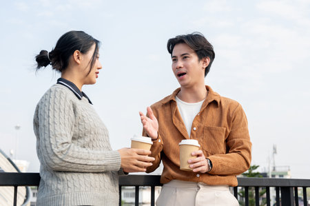 Two serious Asian people, a man and a woman, engage in an intense conversation on the rooftop during a coffee break.の写真素材