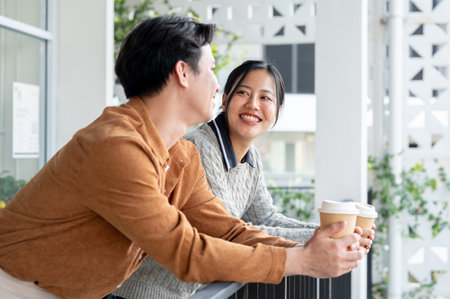 A happy, smiling Asian woman enjoys a conversation with her male colleague on the office balcony during a coffee break.の写真素材