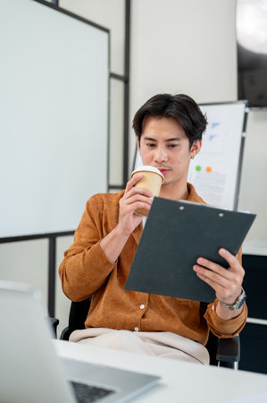 An Asian male office worker focuses on reading a document at his desk in the office.の写真素材