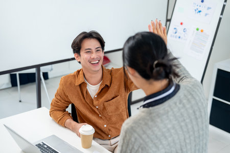 A cheerful, smiling Asian man gives a high five to his colleague to celebrate and cheer up after their project's success.の写真素材