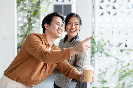A lovely Asian office couple enjoys a conversation and gazes at the view on the balcony during a coffee break, playfully flirting at their workplace.の写真素材