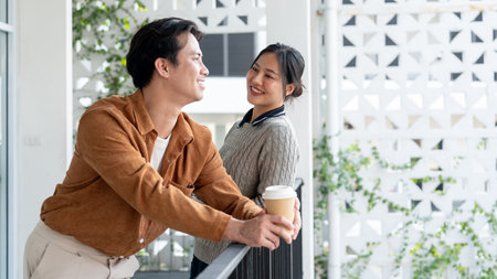 A happy, smiling Asian woman enjoys a conversation with her male colleague on the office balcony during a coffee break.の写真素材