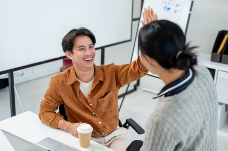 A cheerful, smiling Asian man gives a high five to his colleague to celebrate and cheer up after their project's success.の写真素材