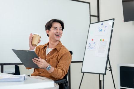 A positive, friendly Asian businessman is waving and smiling at his colleague to say hi while sitting in the office. businesspeople conceptの写真素材