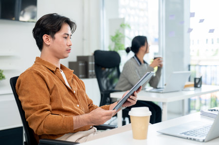 A smart Asian male office worker focuses on reading a document at his desk in the office.の写真素材