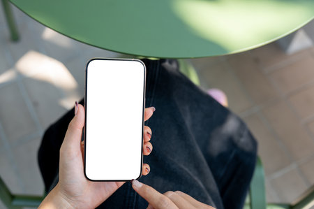 A top view of a woman holding a smartphone with a white screen mockup, using the smartphone while sitting outdoors. people and wireless technology conceptsの写真素材