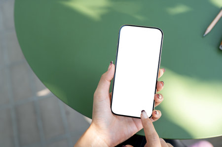 A top view of a woman holding a smartphone with a white screen mockup, using the smartphone while sitting outdoors. people and wireless technology conceptsの写真素材