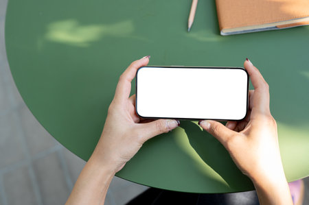 A top view of a woman holding a smartphone in a horizontal position, using a smartphone, watching a video or playing a mobile game while sitting outdoors.の写真素材