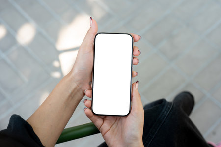 A woman sits outdoors and uses her smartphone. the smartphone with a white screen mockup in a woman's hand. people and wireless technology conceptsの写真素材