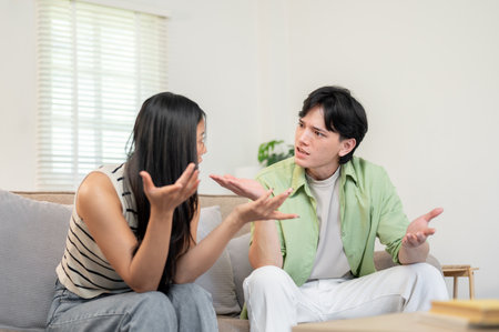 A toxic relationship in a young couple. An unhappy Asian couple sits in the living room, arguing and having a conflict, unable to understand each other.の写真素材