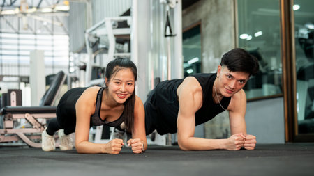 A sporty and athletic Asian male and female, both in sportswear, are performing a plank workout on the gym floor, training together. A supportive Asian couple is working out together in the gym.の写真素材
