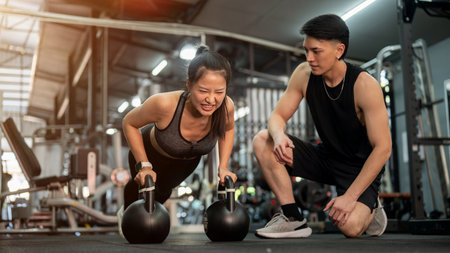 A determined Asian female client is being trained by a professional fitness trainer in the gym,...
