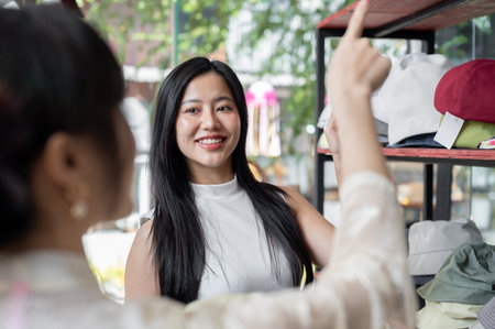 An Asian female customer is pointing at the item on the shelf she wants to buy, showing it to a store employee, and enjoying shopping alone. lifestyle, people, consumerismの写真素材