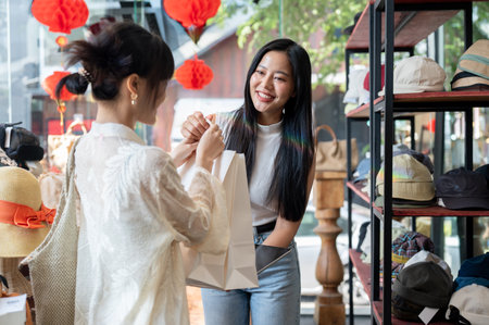 A beautiful, smiling Asian female clothing shop owner or cashier is handing shopping bags to a customer after checkout, creating a pleasant shopping experience in her shop.の写真素材