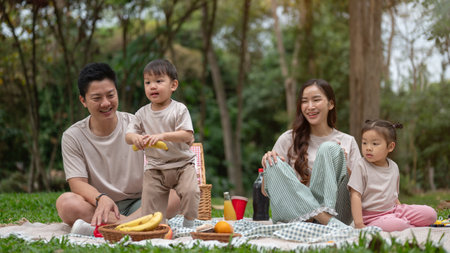 A happy Asian family enjoys a summer picnic in a public park, with mom and dad sharing quality time with their little kids. family, fatherhood, motherhood, childhoodの写真素材