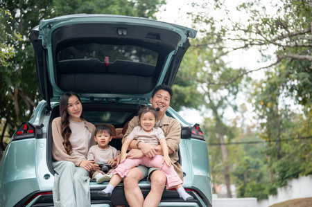 A happy and cheerful Asian family sitting in the trunk of their car, smiling at the camera and enjoying their road trip or camping adventure together. family car, happy moment, travelingの写真素材