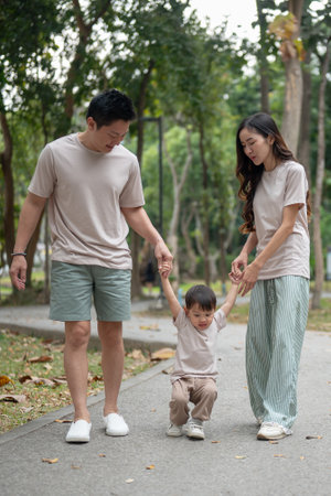 Caring and happy Asian parents hold their son's hand while walking in a public park, enjoying a morning exercise in nature together. outdoor activity, family moment, childhood, parenthoodの写真素材