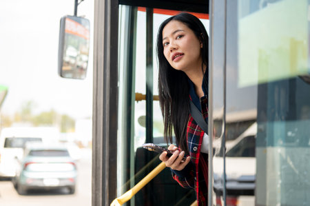 A carefree, positive Asian woman gets off the bus at a bus stop, arriving at her destination while traveling by public transport in the city. people and transportation conceptsの写真素材