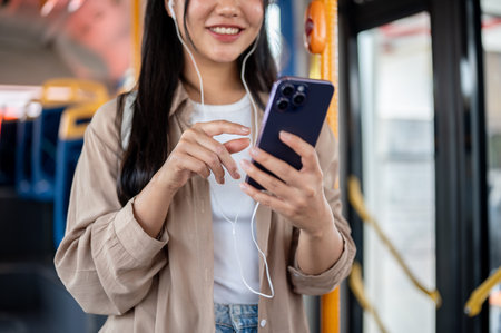 A cropped image of a positive Asian woman in casual clothes enjoys chatting on her smartphone traveling by public bus. people and transportation conceptsの写真素材
