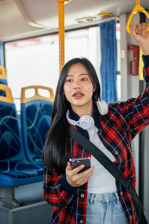 An Asian female college student holds a handrail while riding a bus. city life, public transportation, lifestylesの写真素材