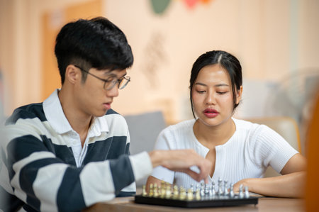 A beautiful Asian woman plays chess seriously with her friend in the living room. leisure, activity, entertainmentの写真素材