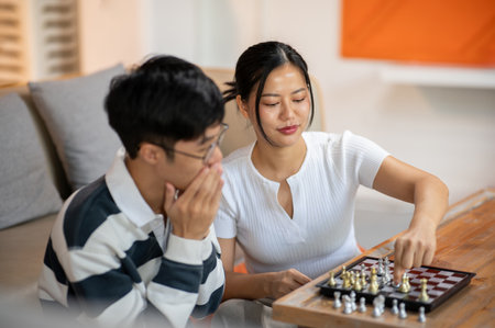 Two happy Asian male and female friends are enjoy playing chess together in the living room. leisure activity, entertainment, board gameの写真素材