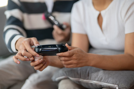 A close-up of two friends, a male and a female, play a video game with joysticks on the sofa in the living room, having a fun time together at home.の写真素材
