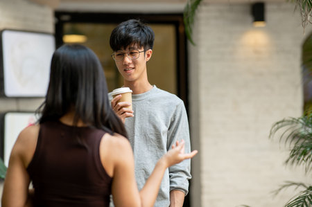 A positive, smiling young Asian man talks to his friend after an unexpected meeting at a coffee shop in the city. people, lifestyles, friendshipの写真素材