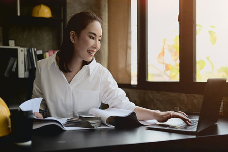 A professional, attractive Asian female architect or engineer manager works at her desk in the...