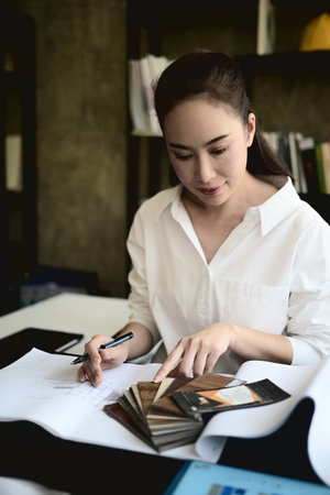 A confident, professional Asian female architect boss works on a building's interior design at her...