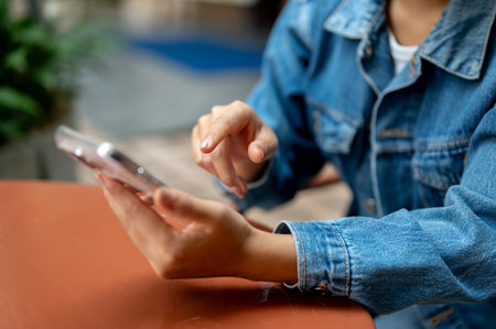 The hand in denim jacket holding a smartphone with left hand and pointing at the screen with right...