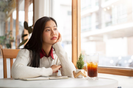 An asian woman is putting her hand under the chin, looking bored or unhappy while waiting for someone at the round marble table.の写真素材