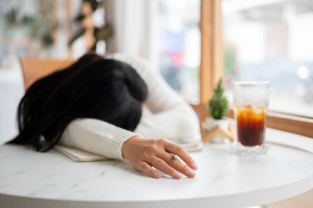 A long hair woman is sleeping or taking a nap while holding a pencil on the marble table in the cafe, with a glass of cold drink place beside.の写真素材