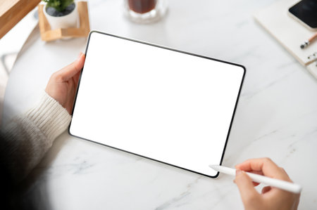 The left hand holding blank screen or white screen tablet with stylus pencil in right hand, sitting at the marble table. Study or Working in the cafe.の写真素材
