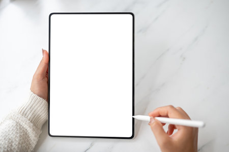 Close up of the blank screen or white screen tablet and stylus pencil holding in the hands, on the empty marble table. Study or Working in the cafe.の写真素材