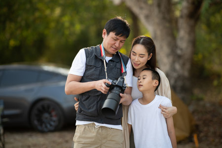 The father is showing the photo he has taken on his camera to mother and son. Family trip, Sightseeing, Forest camping, Outdoor activity.の写真素材