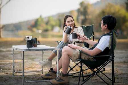 A woman is smiling at the man while pouring drink at folding table, with blurred background of forest scenery. On a date, Travel together, Outdoor activity.の写真素材