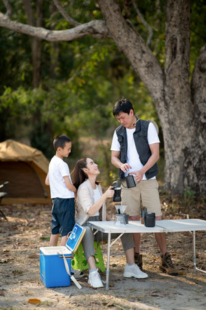 The happy family, Mother and son is smiling while looking at the father holding kettle pouring coffee. Family trip, Forest camping, Outdoor activity.の写真素材