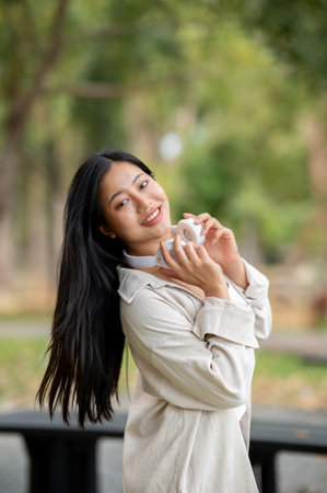 An asian woman is holding headphones and staring into camera while standing in the park, breathing in fresh air. Chilling in nature, Outdoor activity, Greenery park.の写真素材