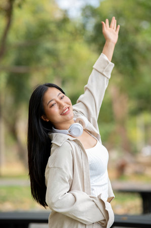 An asian woman is standing with one arm raised and looking ahead in the park, breathing in fresh air. Chilling in nature, Outdoor activity, Greenery forest park.の写真素材