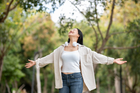 A happy asian woman is standing with open arms in the park, breathing in fresh air. Chilling in nature, Outdoor activity, Greenery forest park.の写真素材