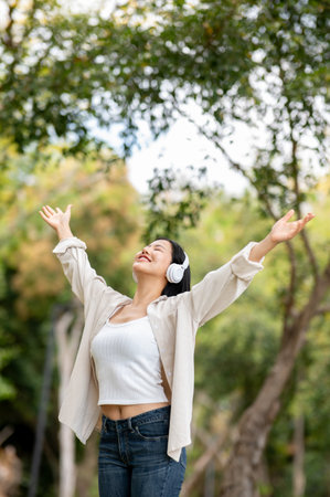 A smiling asian woman is standing with both arms raised, breathing fresh air in the park. Chilling in nature, Outdoor activity, Greenery forest park.の写真素材