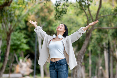 An asian woman is standing with her arms raised, breathing fresh air in the park. Chilling in nature, Outdoor activity, Greenery park.の写真素材