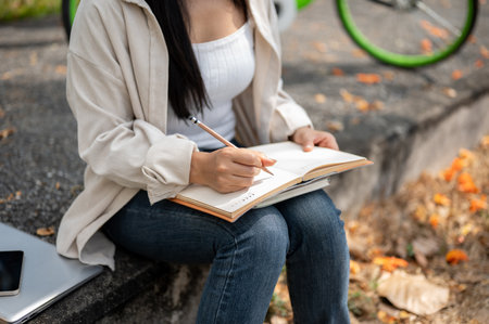 A close up of woman sitting on the sidewalk, writing or drawing in the notebook with a pencil. Study or working outdoor.の写真素材