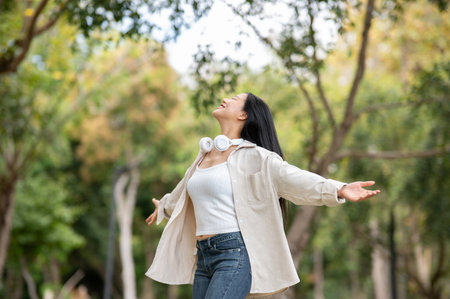 An asian woman is standing with open arms while turning around in the park, breathing in fresh air. Chilling in nature, Outdoor activity, Greenery forest park.の写真素材